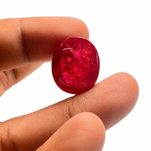 May include: A round, translucent gemstone with a deep red color and visible internal fractures. The stone has a smooth, polished surface and exhibits variations in light reflection across its circular face, highlighting its crystalline structure.