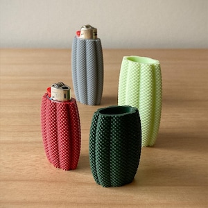 Peut inclure: Quatre étuis décoratifs pour briquets en forme de cactus. Les étuis sont rouges, gris, verts et vert clair. Le support rouge contient un briquet. Les supports sont sur une surface en bois.