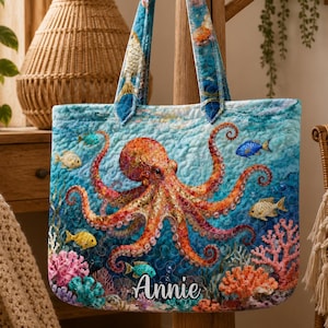 May include: A quilted tote bag with an octopus design. The bag has a blue background with an orange octopus, colourful fish, and coral. The name "Annie" is printed on the bottom. The handles are blue with a fish pattern.