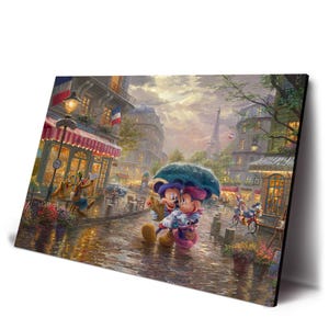May include: A framed art print depicts Mickey and Minnie Mouse embracing under an umbrella in a rainy Parisian street scene. The Eiffel Tower is visible in the background, with shops and cafes lining the cobblestone street. The artwork has a warm, romantic feel.