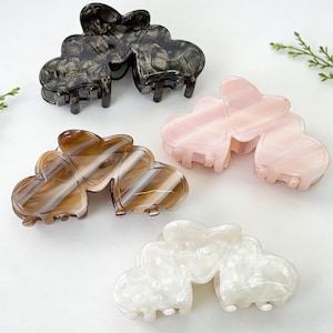 May include: Four heart-shaped hair claw clips in various colours. The clips are in shades of black, pink, brown, and white. Each clip has a marbled effect, adding a touch of elegance. These hair accessories are perfect for adding a stylish touch to any hairstyle.