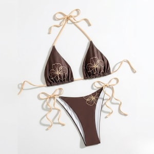 May include: A two-piece brown bikini set with a floral design. The triangle top and the bottoms have a brown base color with a beige floral pattern. The bikini has beige ties.