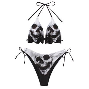 May include: A two-piece bikini set featuring a skull print. The halter top and the bottoms are black and white with a skull graphic. The bikini top has a tie closure at the neck and back. The bottoms have tie closures on each side.