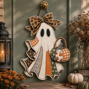 May include: A hanging ghost decoration featuring a patchwork design with various fabric patterns including orange gingham, floral, and chevron prints. The ghost wears a large bow and carries a small pumpkin-shaped basket with a rope handle.