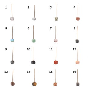 Puede incluir: Una colecci&oacute;n de diecis&eacute;is porta inciensos, cada uno con una base cuadrada de diferente color. Las bases var&iacute;an en color, incluyendo blanco, gris, rosa, azul, verde y marr&oacute;n. Cada soporte tiene un palo delgado y marr&oacute;n que se extiende hacia arriba.