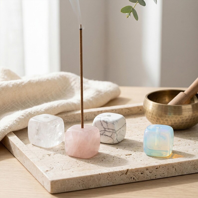 Puede incluir: Conjunto de portainciensos c&uacute;bicos en varios colores: transparente, rosa, blanco y azul. Un palito de incienso encendido en el soporte rosa, con humo ascendente. Un cuenco tibetano de lat&oacute;n y una maza de madera en el fondo.