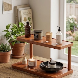 Peut inclure: Une étagère en bois à deux niveaux présente des bougies, un diffuseur et des produits de soin de la peau. L'étagère supérieure contient une bouteille marron, un pot et une bougie en verre. L'étagère inférieure a un plateau noir avec un pot et une bougie.