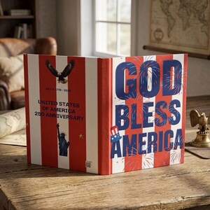 May include: A hardcover book with a red and white striped cover. The front features the text GOD BLESS AMERICA in blue with firework graphics and a top hat icon. The back displays a bald eagle, the Statue of Liberty, and UNITED STATES OF AMERICA 250 ANNIVERSARY.