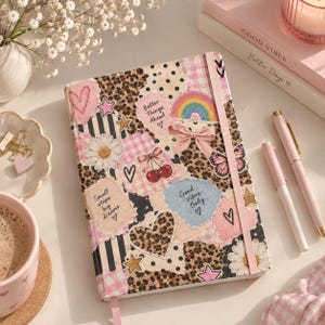 Puede incluir: Un diario de tapa dura con una cubierta estilo collage que presenta estampado de leopardo, rayas blancas y negras y patrones de cuadros vichy rosas. La cubierta está decorada con pegatinas de un arcoíris, cerezas, margaritas, corazones y los textos Better Things Ahead, Small steps big dreams y Good Vibes Only.