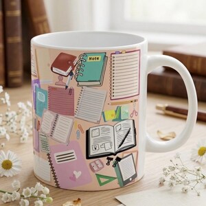 May include: White ceramic mug featuring a repeating pattern of school supplies, including notebooks, pencils, and a calculator, in shades of pink, green, and brown. The mug has a white handle and a light pink background.
