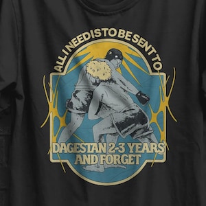 Op de afbeelding: Zwart T-shirt met een afbeelding van twee worstelaars in een blauw en geel ontwerp. De tekst luidt "ALL I NEED IS TO BE SENT TO DAGESTAN 2-3 YEARS AND FORGET". Een gele cirkel met "BUY 3 FREE" staat rechtsboven.