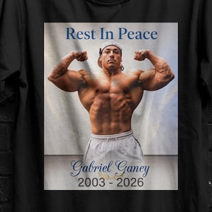 Può includere: T-shirt nero con una grafica di un uomo muscoloso che si flette, con la scritta "Rest In Peace" sopra e "Gabriel Ganey 2003-2026" sotto. La maglietta ha anche un piccolo logo in alto a sinistra.