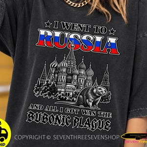 Può includere: Una t-shirt a maniche corte grigio antracite con una stampa grafica recante il testo I WENT TO RUSSIA AND ALL I GOT WAS THE BUBONIC PLAGUE. Il design include un'illustrazione dettagliata della Cattedrale di San Basilio e un castoro in bianco.