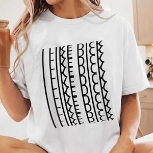 Puede incluir: Una camiseta blanca de manga corta con un diseño gráfico negro en la parte delantera. El diseño consiste en líneas verticales y el texto repetido "I LIKE DICK" dispuesto en formato de columna. La camiseta tiene cuello redondo y corte estándar.