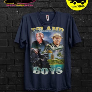 Puede incluir: Camiseta azul marino con un dise&ntilde;o gr&aacute;fico con el texto "ISLAND BOYS" e im&aacute;genes de tres hombres. El dise&ntilde;o incluye una escena de isla tropical con palmeras y un edificio. La camiseta tiene cuello redondo.