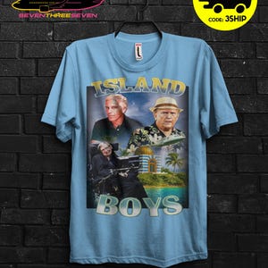 Puede incluir: Camiseta azul claro con un dise&ntilde;o gr&aacute;fico con el texto "ISLAND BOYS" e im&aacute;genes de tres hombres. La camiseta tambi&eacute;n tiene un logotipo de avi&oacute;n amarillo y negro y una promoci&oacute;n "COMPRA 3 GRATIS".