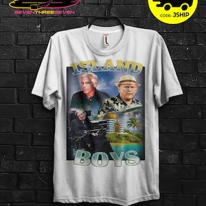 Puede incluir: Camiseta blanca con un dise&ntilde;o gr&aacute;fico que presenta el texto "ISLAND BOYS" e im&aacute;genes de tres hombres. El dise&ntilde;o incluye una escena tropical con palmeras y un edificio. La camiseta tiene cuello redondo.