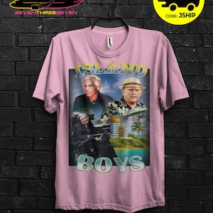Puede incluir: Camiseta rosa claro con un dise&ntilde;o gr&aacute;fico que presenta el texto "ISLAND BOYS" e im&aacute;genes de tres hombres. El dise&ntilde;o incluye una escena tropical con palmeras y un edificio. La camiseta tambi&eacute;n tiene el texto "SEVENTHREESEVEN" y un avi&oacute;n.