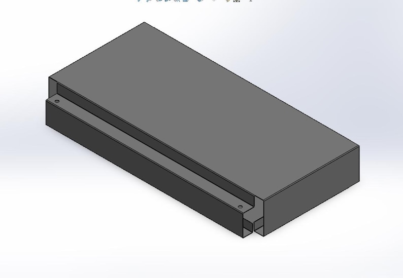 May include: A rectangular, gray, 3D-modeled object with a recessed channel running along one side. The object has a solid, block-like appearance with a consistent color and texture throughout. The design is simple and geometric.