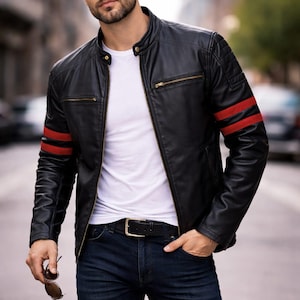 May include: A black leather jacket featuring a mandarin collar, gold-tone zips, and two horizontal red stripes on each sleeve. The jacket is worn over a plain white t-shirt paired with dark blue denim jeans and a black leather belt with a metal buckle.