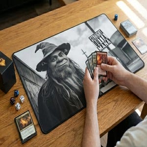 May include: A black and white gaming mousepad featuring a wizard-like character with the text "STRAIGHT OUTTA MANA". The image includes dice, playing cards, and a card deck box, suggesting a tabletop gaming theme.