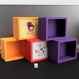 May include: A display of colorful, cube-shaped storage boxes in orange, yellow, and purple. The boxes feature decorative patterns and contain items with "ONE PIECE" branding. A white die with black dots sits in front.