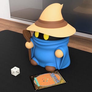 Op de afbeelding: Een blauw beeldje van een magiër met een gele hoed en staf, naast een dobbelsteen en een Magic-kaart. De magiër heeft gele ogen en een bruine staf. Op de kaart staat het woord "Magic".