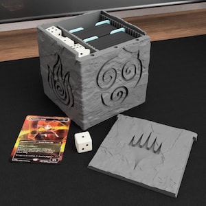May include: A gray, stone-textured card and dice storage box with carved symbols and a removable lid. The box holds cards, dice, and a trading card. The card features an illustration of a character. A white die is next to the box.