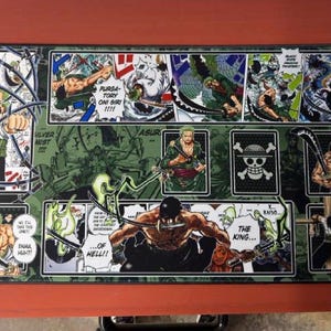 Może przedstawiać: Prostokątna czarno-zielona podkładka pod mysz z ilustracjami w stylu mangi postaci z zielonymi włosami i mieczami. Podkładka ma dymki z tekstem i symbol czaszki.