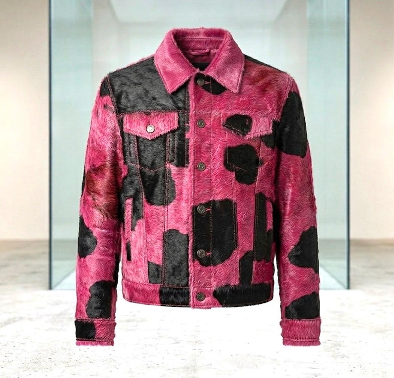 May include: A long-sleeve jacket featuring a vibrant pink and black cow-print pattern with a textured fur-like finish. The garment includes a classic collar, a front button-down closure with metallic buttons, and two chest pockets with buttoned flaps.