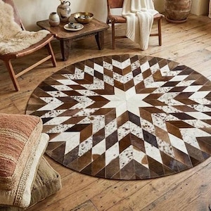 May include: A circular area rug featuring a geometric starburst pattern composed of individual cowhide patches in shades of brown, white, and dark brown. The design consists of alternating diamond-shaped segments radiating from the centre.