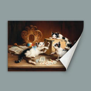 May include: A vintage print depicting three kittens with black and white markings at play. One kitten reaches for a wooden box, while another interacts with playing cards. A colourful ball and open book add to the scene's charm. The background has a dark, warm tone.