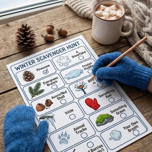May include: A winter scavenger hunt checklist with illustrations and tick boxes. The list includes items like a pinecone, snowflake, and red berries. A person wearing blue mittens is marking the checklist with a pencil. A mug of hot chocolate and a cosy sweater are nearby.