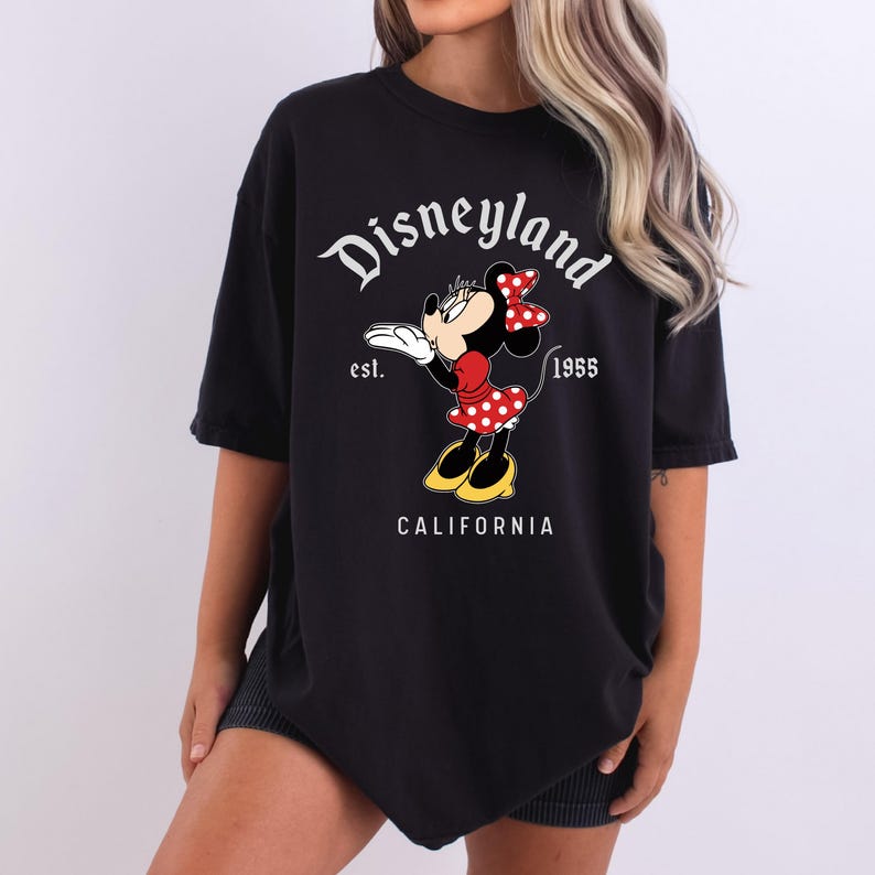 May include: Black t-shirt featuring a graphic of Minnie Mouse blowing a kiss, with the text "Disneyland" above and "California" below. The design includes the year "1955" and the word "est."
