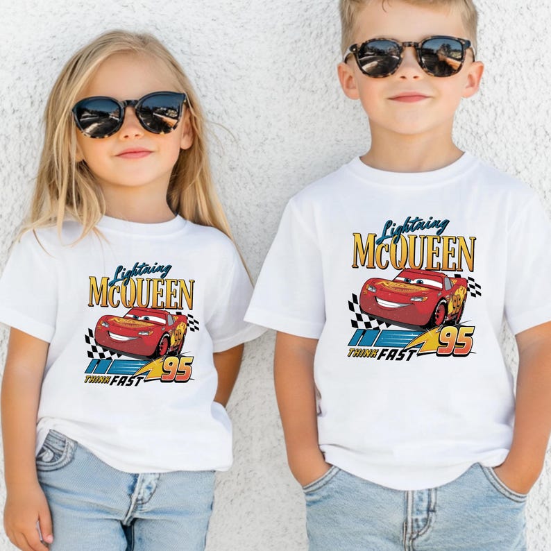 May include: Two children wearing white t-shirts featuring Lightning McQueen from the Cars movie. The shirts have a red car graphic with the text "Lightning McQueen" and "Think Fast 95". Both children are wearing sunglasses.