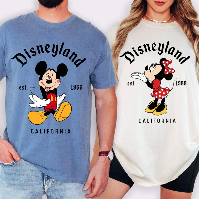 May include: Two t-shirts featuring the Disneyland logo and cartoon characters Mickey and Minnie Mouse. The blue shirt has Mickey Mouse, and the white shirt has Minnie Mouse. Both shirts have the text "est. 1955 CALIFORNIA".