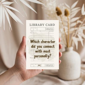 May include: A beige library card with the text "Which character did you connect with most personally?" is held in a hand. The card has a vintage design with lines and numbers. Dried flowers and a vase are in the background.
