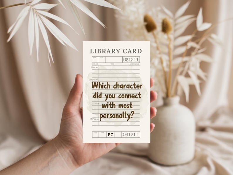 May include: A beige library card with the text "Which character did you connect with most personally?" is held in a hand. The card has a vintage design with lines and numbers. Dried flowers and a vase are in the background.