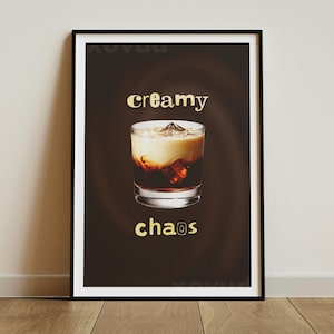 May include: A framed print featuring a cocktail in a rocks glass with ice. The drink has layers of dark and light colors. The words "creamy" and "chaos" are in gold lettering on a dark brown background.