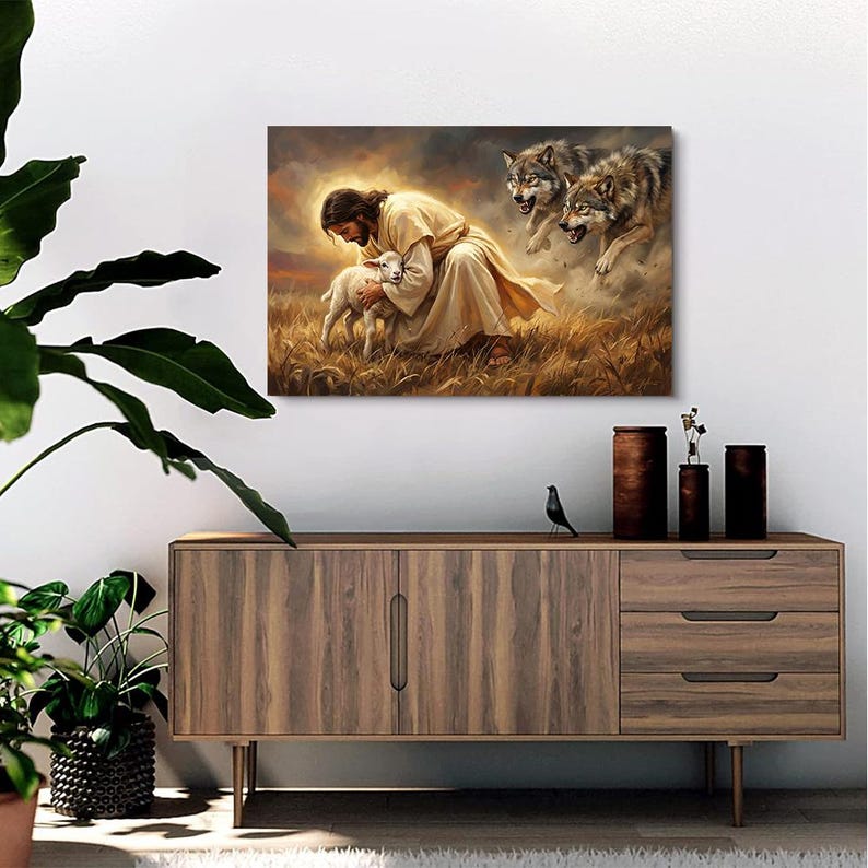 May include: A canvas print depicting a religious scene. A figure in a cream-colored robe cradles a lamb in a field of wheat. Two wolves are in the background, with a cloudy sky. The artwork is displayed above a wooden cabinet.