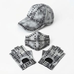 Puede incluir: Una gorra de b&eacute;isbol, una mascarilla y un par de guantes sin dedos con un acabado gris y negro lavado al &aacute;cido. Cada art&iacute;culo presenta un aspecto moteado y est&aacute; decorado con numerosas peque&ntilde;as p&uacute;as met&aacute;licas negras dispuestas en filas.