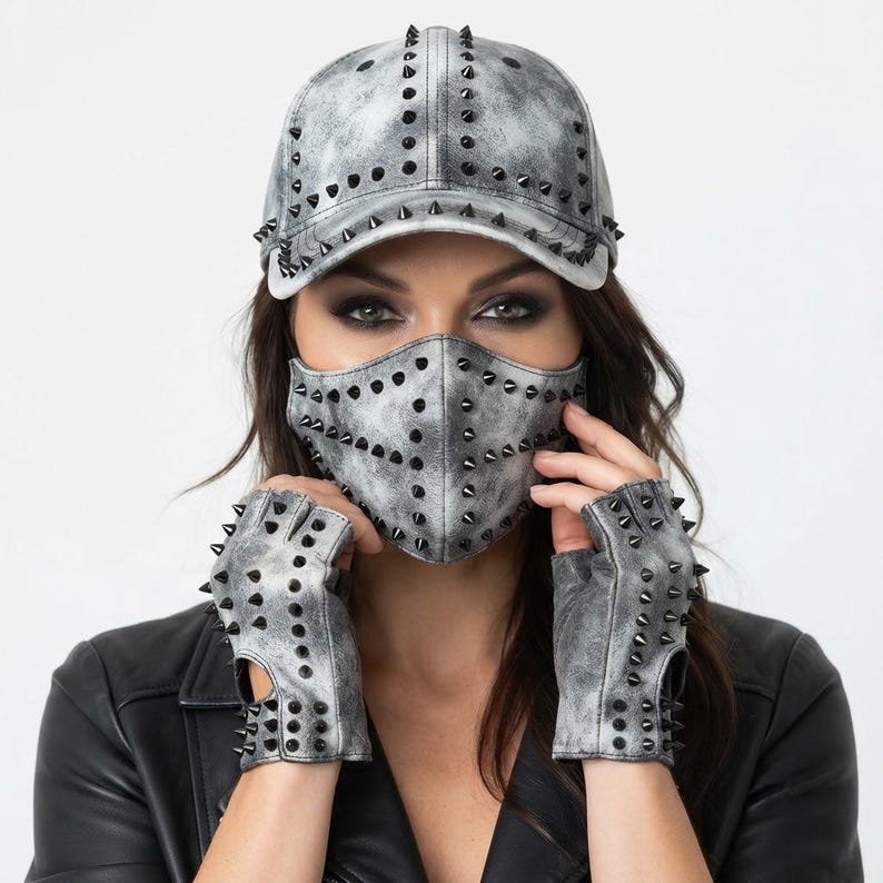 Puede incluir: Una gorra de b&eacute;isbol, una mascarilla y guantes sin dedos con un acabado gris y negro desgastado. Cada art&iacute;culo presenta una textura envejecida y est&aacute; adornado con numerosos remaches met&aacute;licos negros y afilados dispuestos en un patr&oacute;n de rejilla.