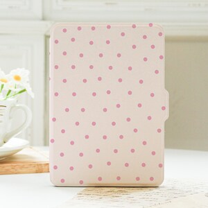 May include: A rectangular e-reader case in a light cream color featuring a scattered pattern of small, solid pink polka dots. The case has a smooth, flat surface with a distinct notched edge on the right side, designed to fit a handheld electronic device.
