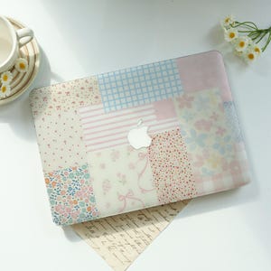 May include: A laptop hard shell case featuring a patchwork design of various pastel patterns including light blue grid, pink stripes, small floral prints, and ribbon motifs, with a central cutout revealing the silver Apple logo on the laptop lid.
