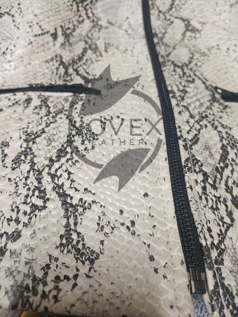 K&ouml;nnte beinhalten: Nahaufnahme einer Jacke mit Schlangenmuster in Wei&szlig;-, Grau- und Schwarzt&ouml;nen. Die Jacke hat einen schwarzen Rei&szlig;verschluss und den Text "OVEX LEATHER". Die Textur des Materials ist sichtbar.
