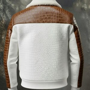 Puede incluir: Chaqueta blanca con detalles en piel de cocodrilo sintética marrón en los hombros y las mangas. La chaqueta tiene un patrón blanco texturizado y un cuello blanco y esponjoso. Los puños y el dobladillo son acanalados.