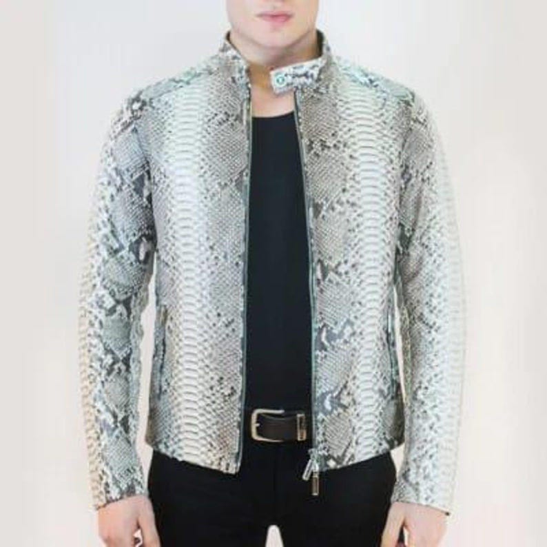 K&ouml;nnte beinhalten: Eine Jacke mit Schlangenmuster mit Stehkragen und durchgehendem Rei&szlig;verschluss. Die Jacke ist &uuml;berwiegend grau und wei&szlig;, darunter ist ein schwarzes Hemd zu sehen. Das Model tr&auml;gt eine schwarze Hose und einen schwarzen G&uuml;rtel mit silberner Schnalle.