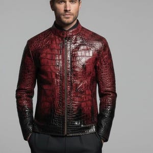 May include: A long-sleeved jacket featuring a textured, glossy crocodile skin pattern in a deep red color that transitions to black at the cuffs and hem. The jacket has a high mandarin collar, a central vertical zipper, and a black shirt underneath.