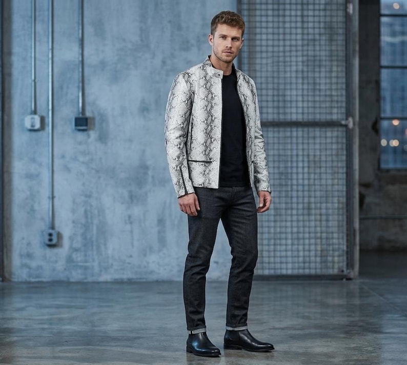 K&ouml;nnte beinhalten: Eine wei&szlig;-graue Jacke mit Schlangenmuster und schwarzem Besatz. Die Jacke wird &uuml;ber einem schwarzen T-Shirt getragen und mit dunkelgrauen Jeans und schwarzen Stiefeln kombiniert. Das Outfit wird durch einen schwarzen G&uuml;rtel erg&auml;nzt.