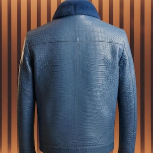 Puede incluir: Chaqueta de cuero azul con un patrón de cocodrilo texturizado. La chaqueta tiene un cuello de piel azul y se muestra en un maniquí. La vista trasera revela las costuras y los detalles del diseño. Una prenda de abrigo elegante.